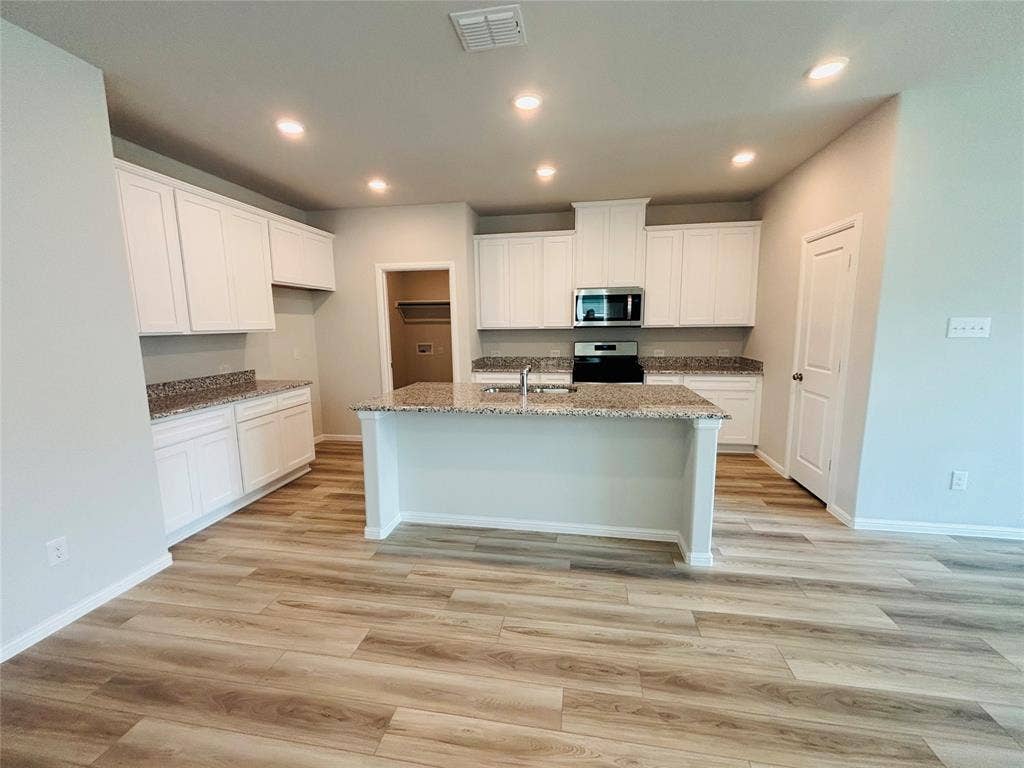 912 Santa Lucia Drive, Anna, TX 75409 Kitchen with stainless steel microwave, stove, light stone counters, an island with sink, and light wood-type flooring