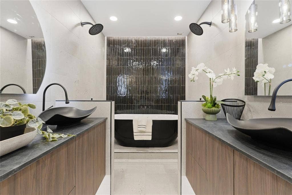 Modern bathroom featuring a freestanding soaking tub, dual shower heads, and twin wood-finish vanities with black vessel sinks