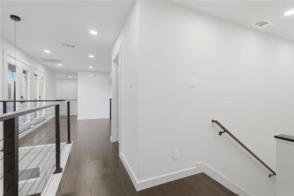 Upper-level hallway featuring dark wood-finish flooring, recessed lighting, white walls, and a contemporary cable railing system