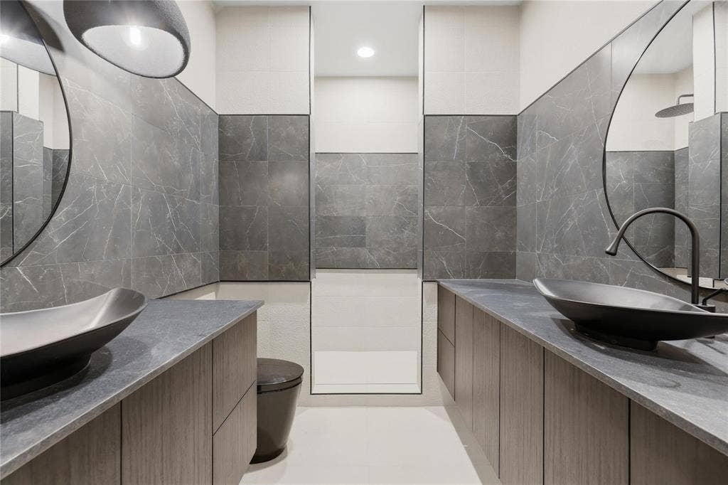 Dual floating vanities featuring wood-finish cabinetry, dark stone countertops, and vessel sinks with matte black fixtures