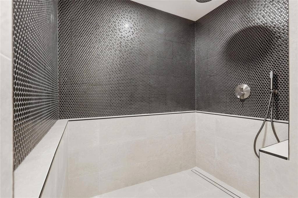 Shower enclosure featuring dark penny tile accent wall, light-toned large format ceramic wall tiles, recessed linear drain, brushed nickel shower controls, and a handheld showerhead