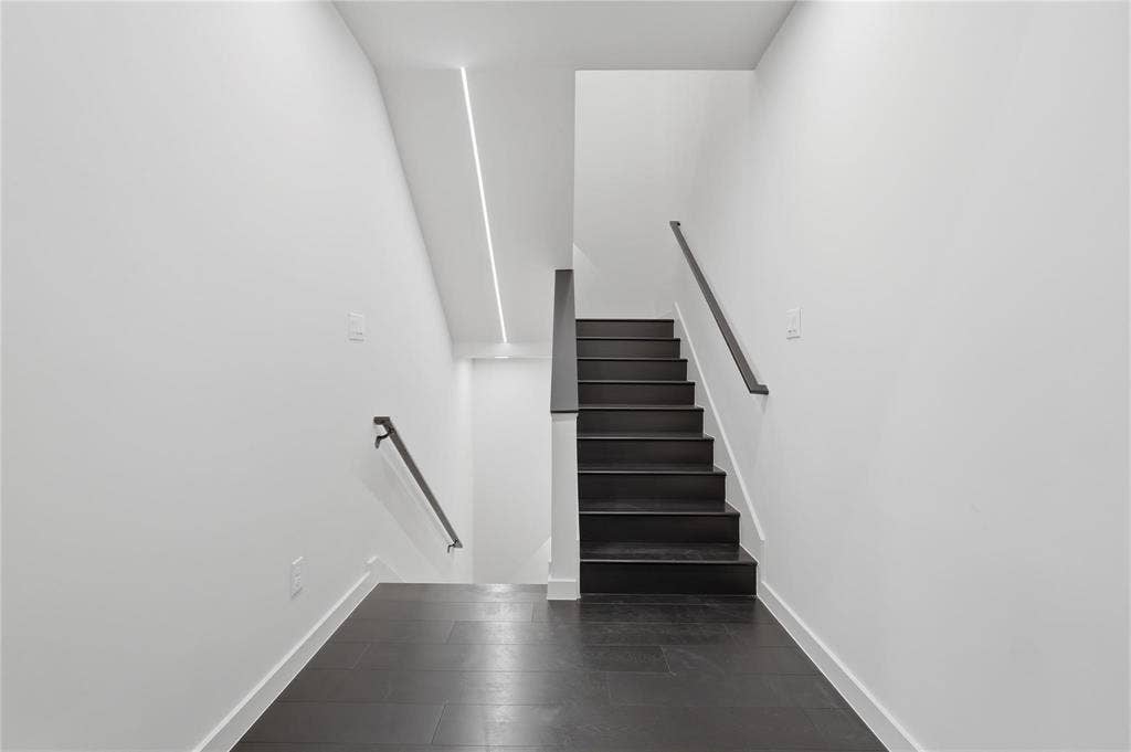 Stairwell featuring dark wood-finish flooring and stairs, white walls, black handrails, and recessed linear ceiling lighting