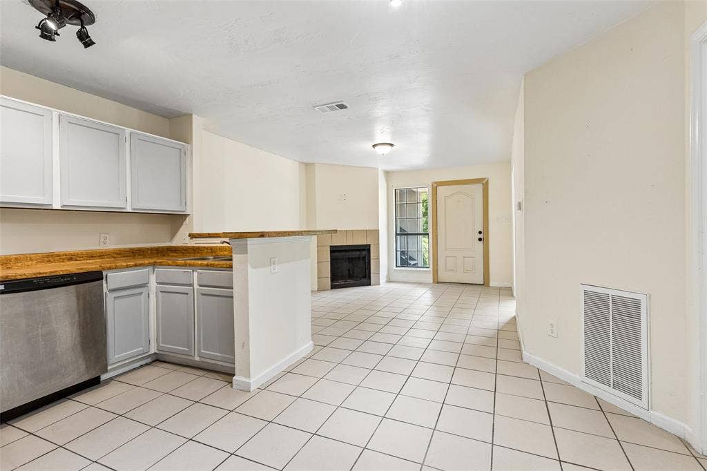 6108 Abrams Road, #610, Dallas, TX 75231 Open-concept living space with tile flooring, a fireplace, and a kitchen featuring white cabinetry, a breakfast bar, and a stainless steel dishwasher