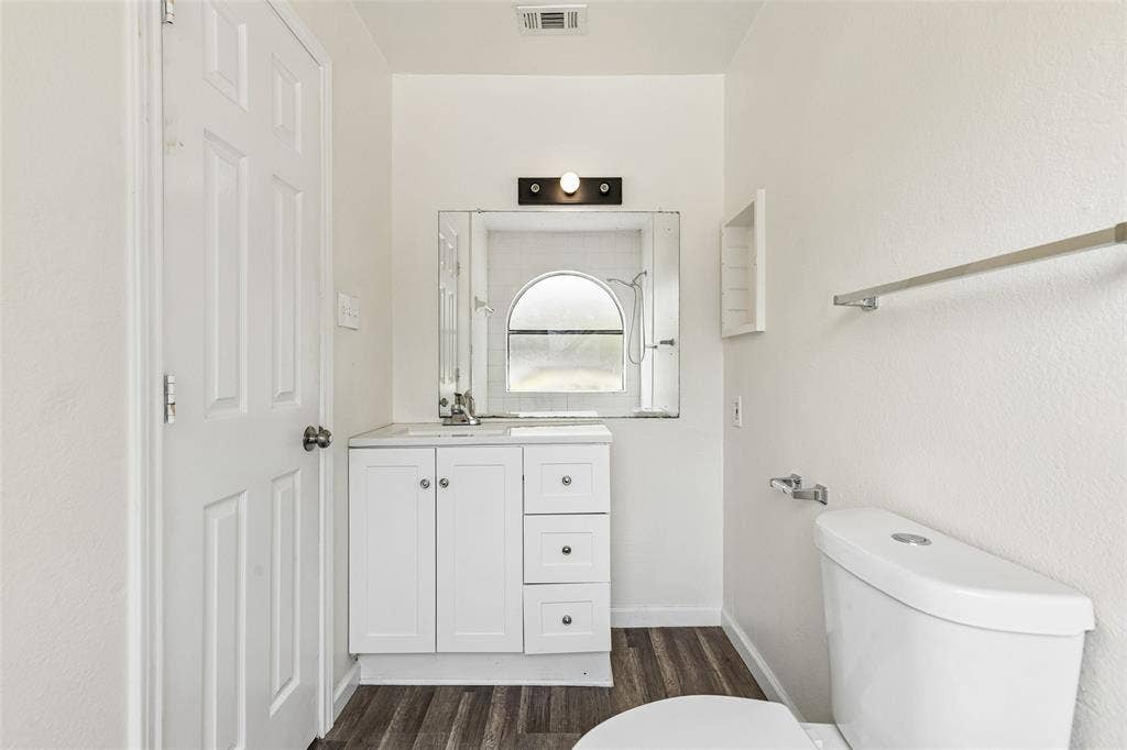6108 Abrams Road, #610, Dallas, TX 75231 Bathroom featuring a white vanity with integrated sink, chrome faucet, wall-mounted mirror, and wood-finish flooring