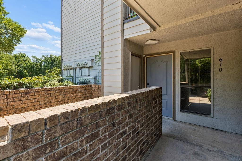 6108 Abrams Road, #610, Dallas, TX 75231 Brick privacy wall framing an entryway with a light-toned door, an adjacent window, and concrete flooring