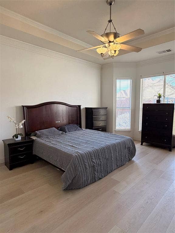 2301 Clearspring Drive S, Irving, TX 75063 Spacious primary bedroom downstairs, featuring light wood-finish flooring, a tray ceiling with crown molding, and a ceiling fan with integrated lighting