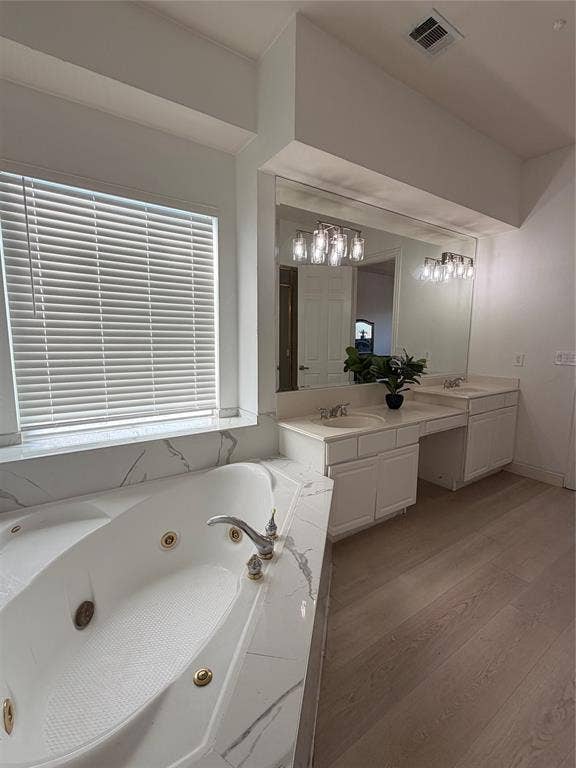 2301 Clearspring Drive S, Irving, TX 75063 Bathroom featuring a built-in jetted tub with a marble-look surround, dual vanity with undermount sinks, and wood-finish flooring