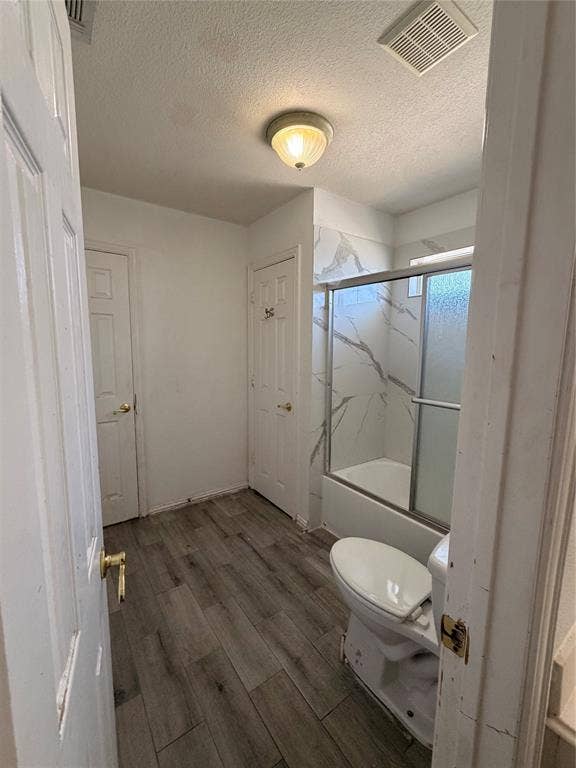 2301 Clearspring Drive S, Irving, TX 75063 Bathroom featuring a shower/tub combination with patterned tile surround and sliding glass doors, a white toilet, and wood-finish flooring