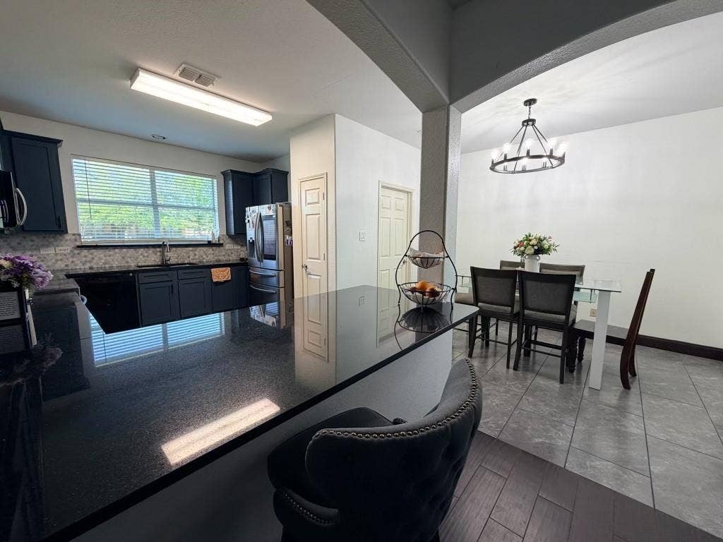Kitchen featuring dark cabinetry, dark countertops, a tile backsplash, and a stainless steel refrigerator