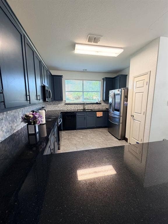 Modern kitchen featuring dark cabinetry, dark speckled countertops, a mosaic tile backsplash, stainless steel refrigerator, and recessed lighting