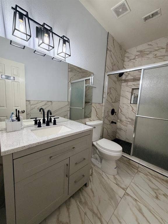 Bathroom featuring a white vanity with a light speckled countertop, matte black fixtures, a shower with sliding glass doors and black hexagon tile flooring, and large format marbled wall and floor tiles