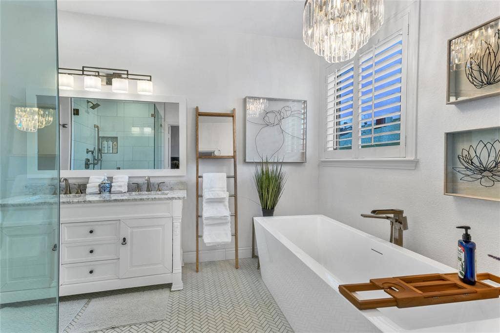 Bathroom featuring a freestanding soaking tub with floor-mounted faucet, a double vanity with stone countertop, and a glass-enclosed shower