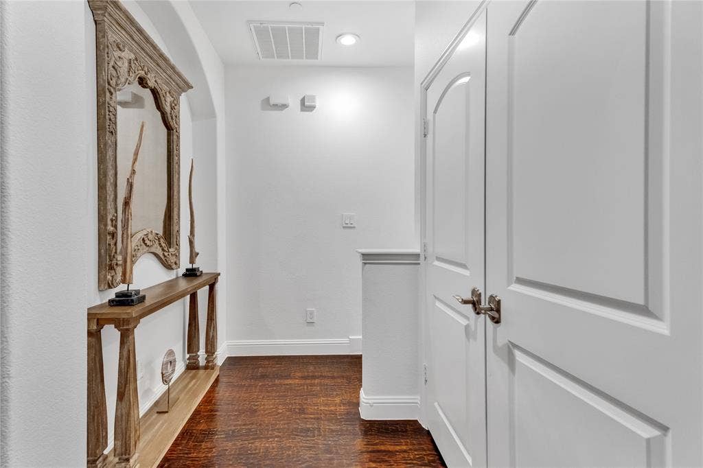 Hallway with wood-finish flooring, white paneled doors, and arched architectural detailing