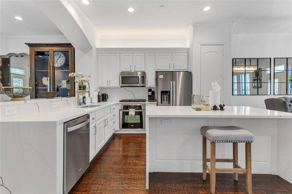 Gourmet kitchen featuring white shaker cabinetry, stainless steel appliances, quartz countertops, a breakfast bar, and wood-finish flooring