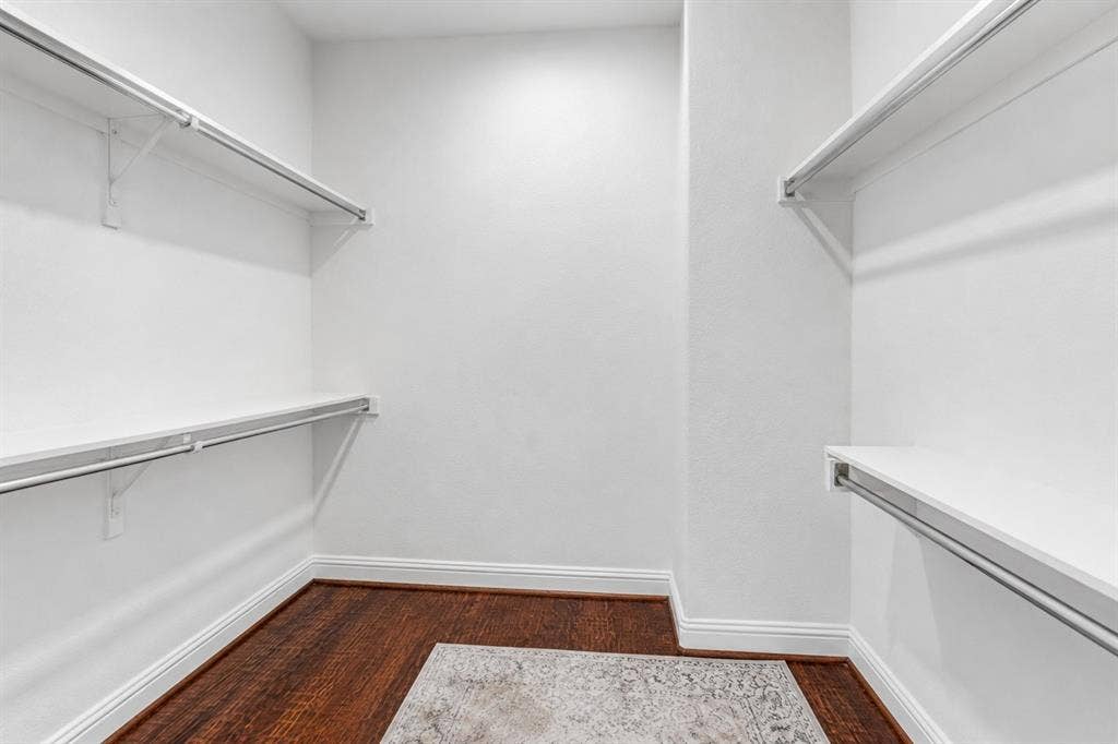 Walk-in closet featuring white shelving with chrome hanging rods, dark wood-finish flooring, and white baseboards