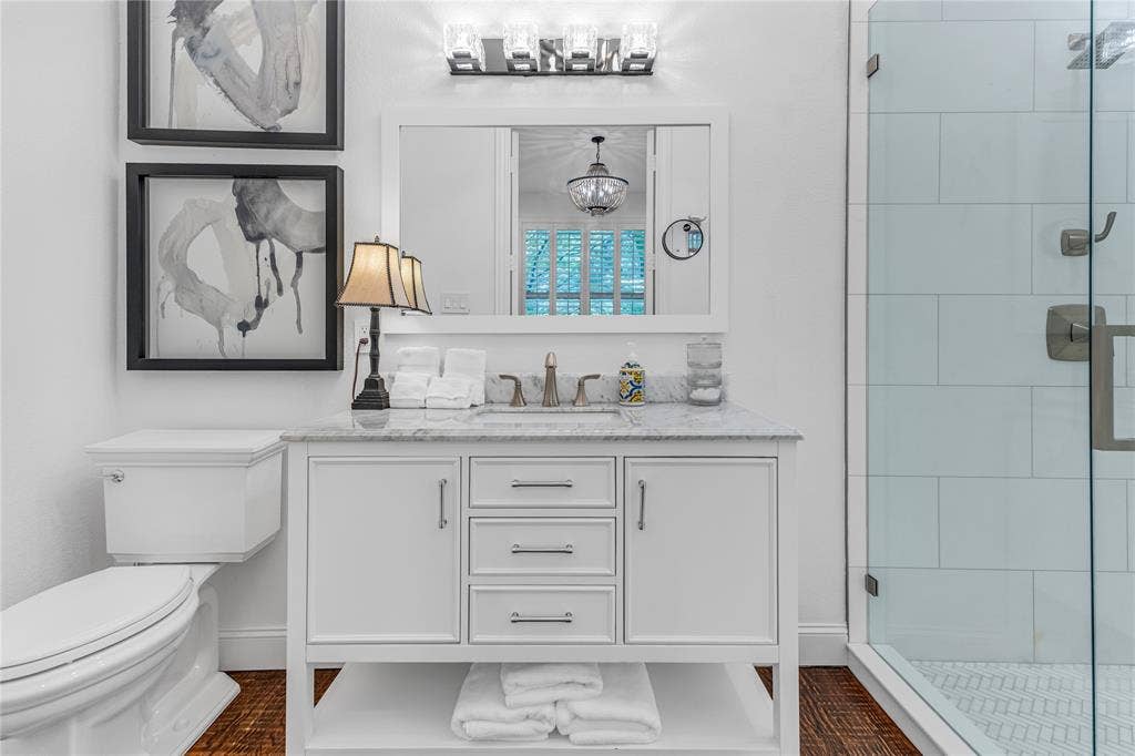 White vanity with a stone countertop, chrome fixtures, and a frameless glass shower enclosure