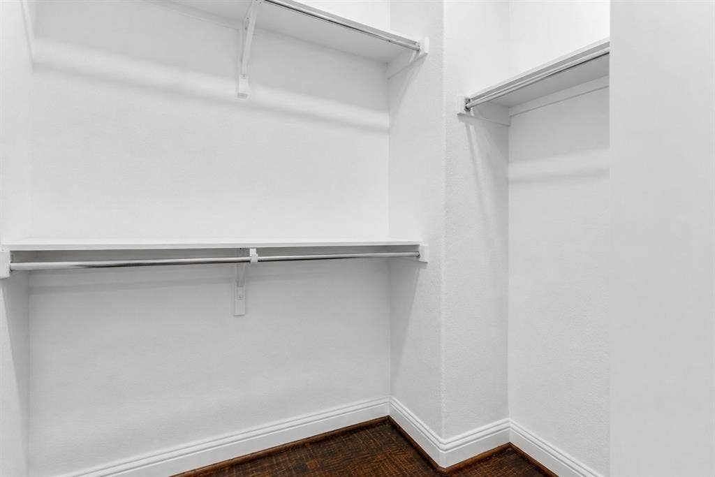 Walk-in closet featuring white wire shelving, chrome hanging rods, wood-finish flooring, and white baseboards