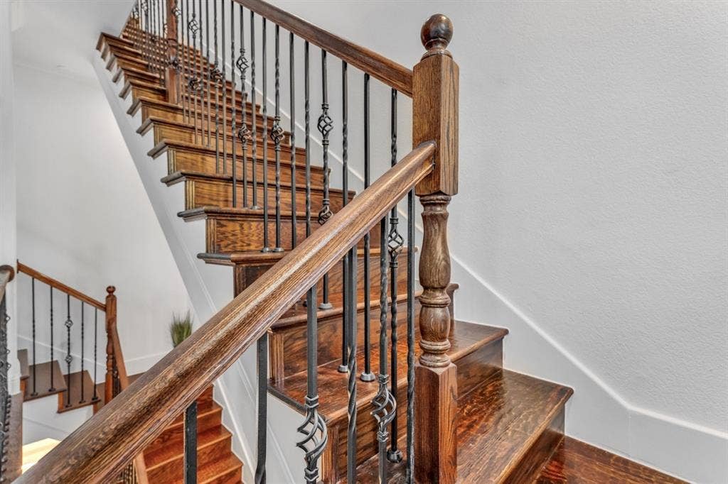 Staircase featuring dark wood treads and risers, wrought iron balusters with decorative twists, a substantial wood newel post, and a matching wood handrail