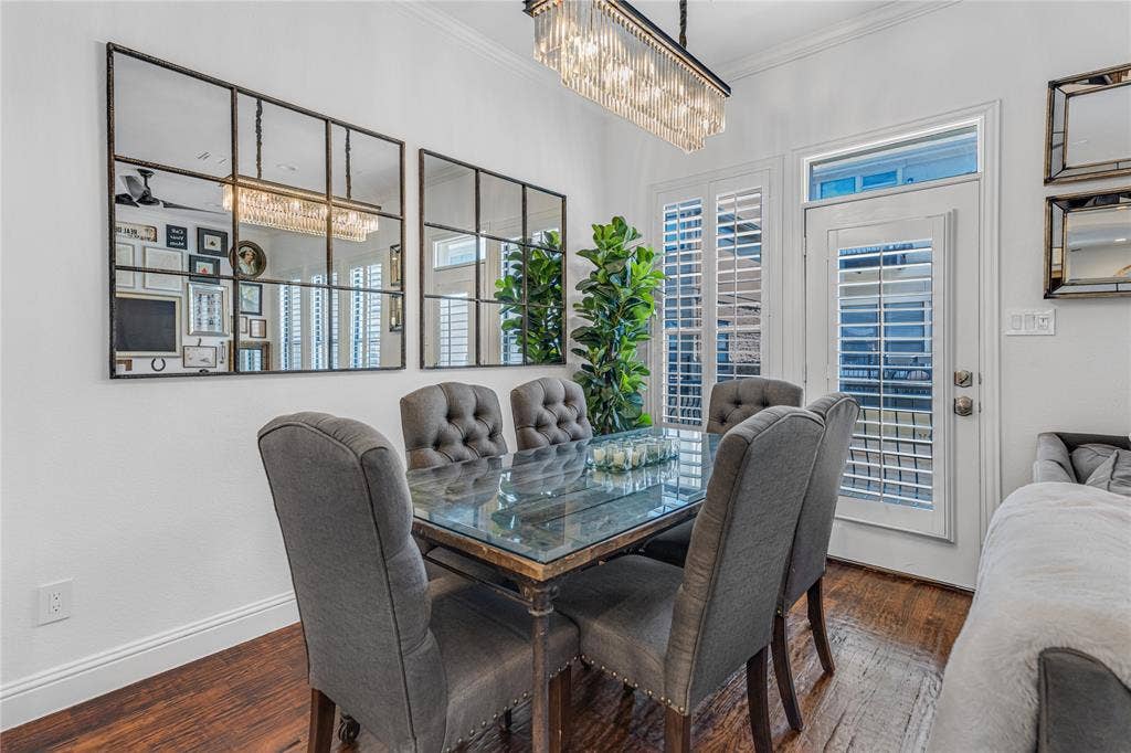 Dining area featuring rich wood-finish flooring, a contemporary chandelier, two panel mirrors, and a door with an upper transom window