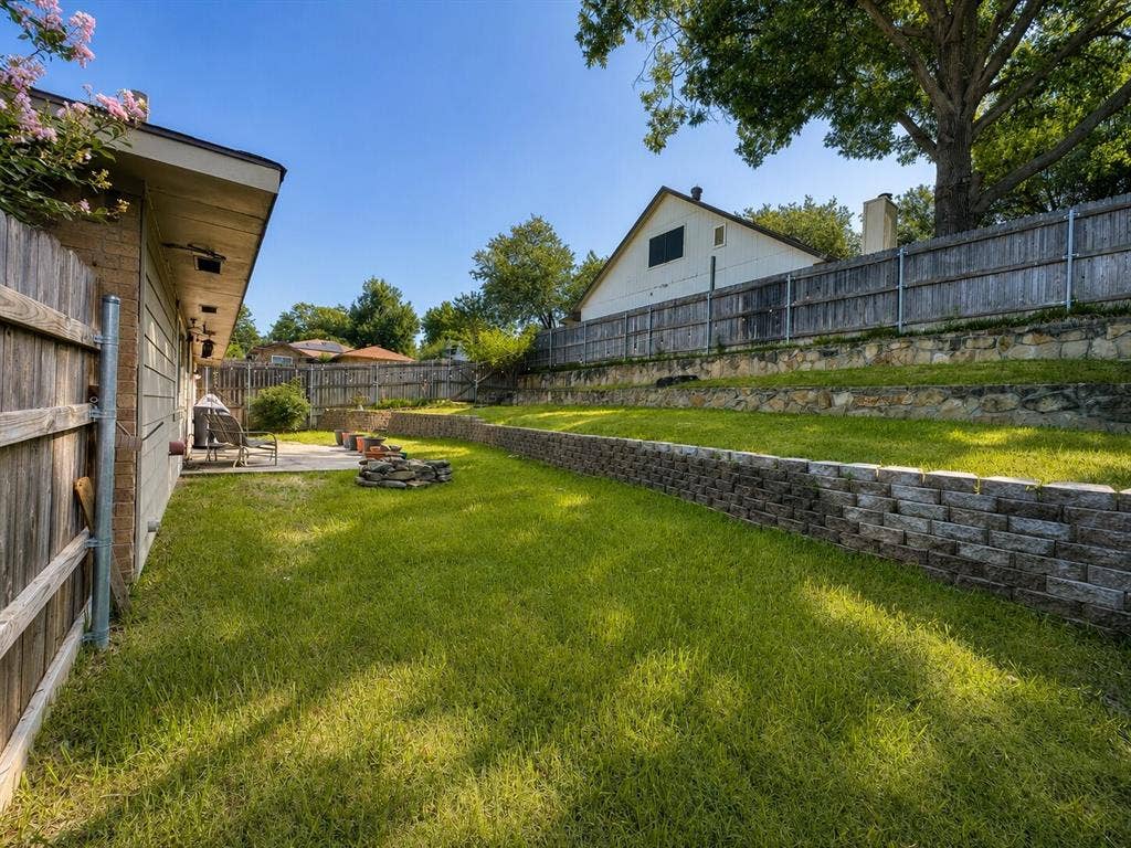 601 Ascot Drive, Euless, TX 76040 Expansive backyard featuring a concrete patio, tiered retaining walls, and a wood privacy fence