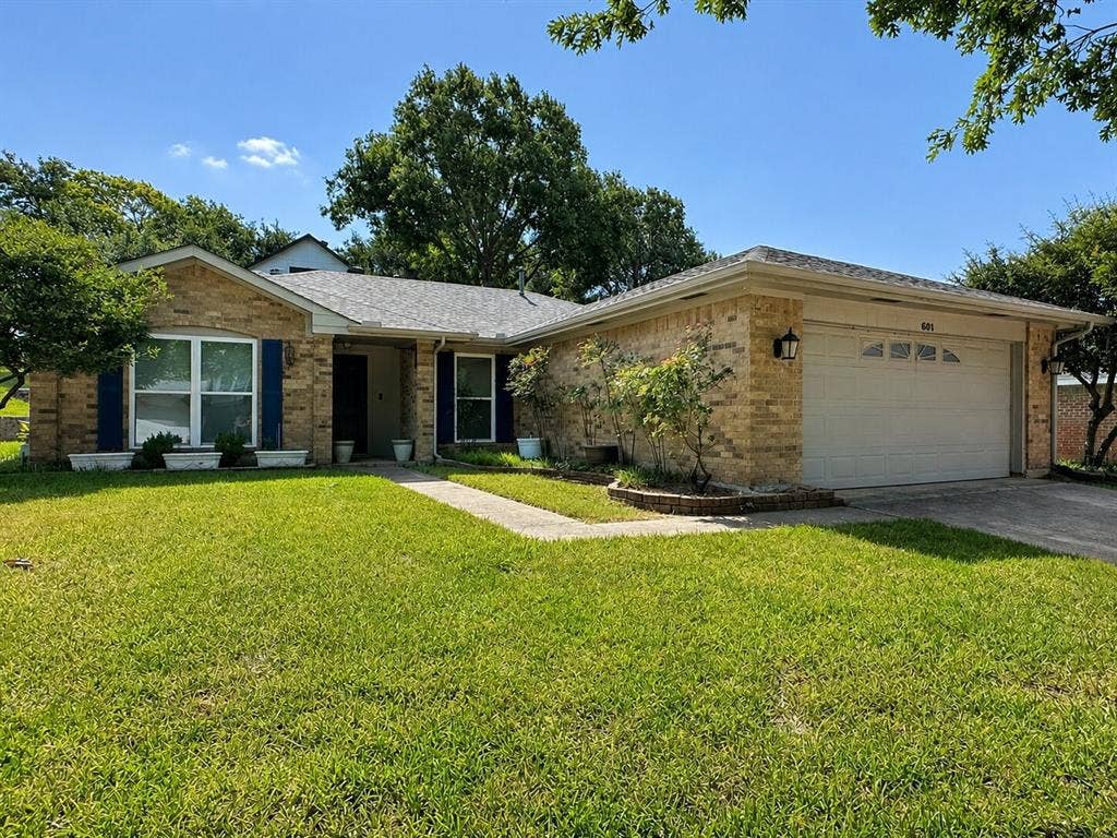 601 Ascot Drive, Euless, TX 76040 Single-story residence featuring a light brick exterior, a two-car garage with a panel door, and blue louvered shutters