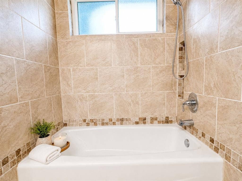601 Ascot Drive, Euless, TX 76040 Bathtub with light-toned wall tiling, mosaic accent banding, a frosted window, and chrome fixtures