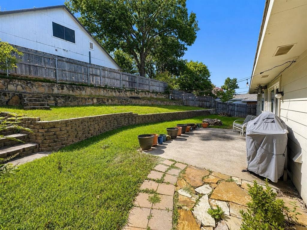 601 Ascot Drive, Euless, TX 76040 Multi-tiered backyard featuring a concrete patio, stone slab pathway, and terraced lawn areas with retaining walls