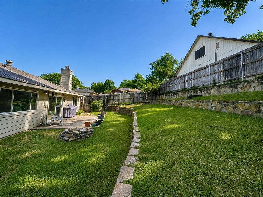601 Ascot Drive, Euless, TX 76040 Expansive backyard featuring a tiered lawn, stone retaining walls, and a private patio area