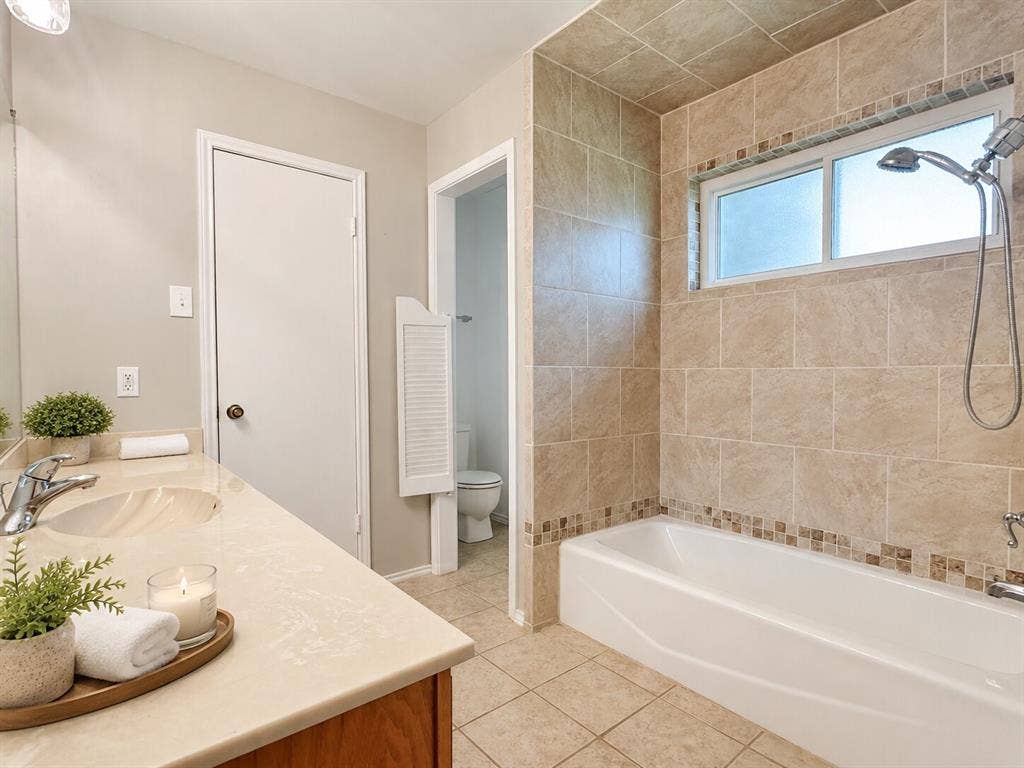 601 Ascot Drive, Euless, TX 76040 Bathroom featuring a double vanity with integrated sinks, a built-in bathtub with a showerhead, and a tiled surround with a decorative mosaic accent