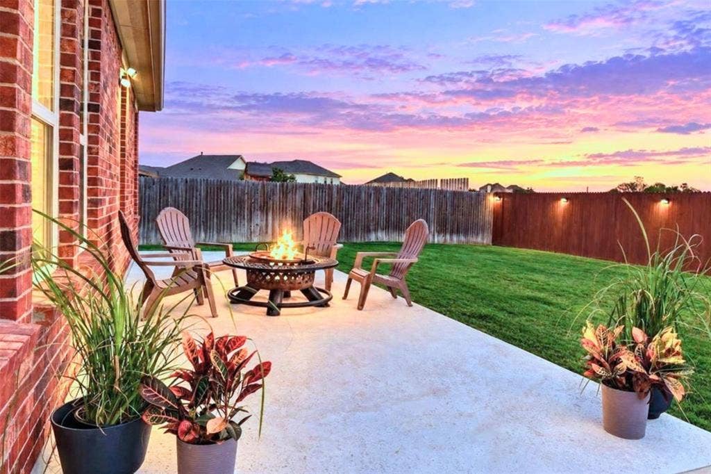 Brick exterior with a concrete patio, a manicured lawn, and a wooden privacy fence with integrated lighting