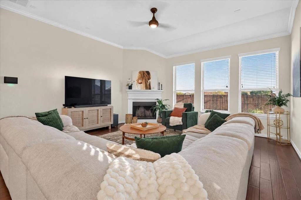 Hardwood-style flooring, white crown molding, a built-in fireplace with a mantel, and three large windows with blinds