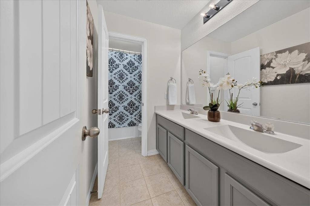 Double vanity with integrated sinks, gray shaker-style cabinetry, and a large wall-mounted mirror