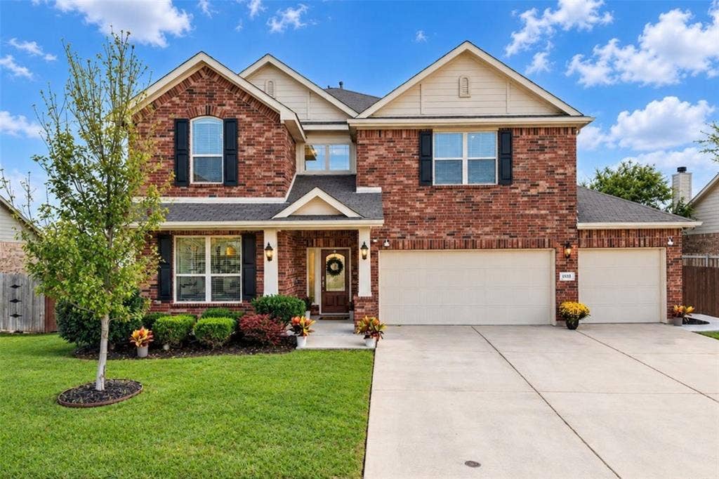Brick facade, attached two-car garage, concrete driveway, front entry porch, and manicured landscaping