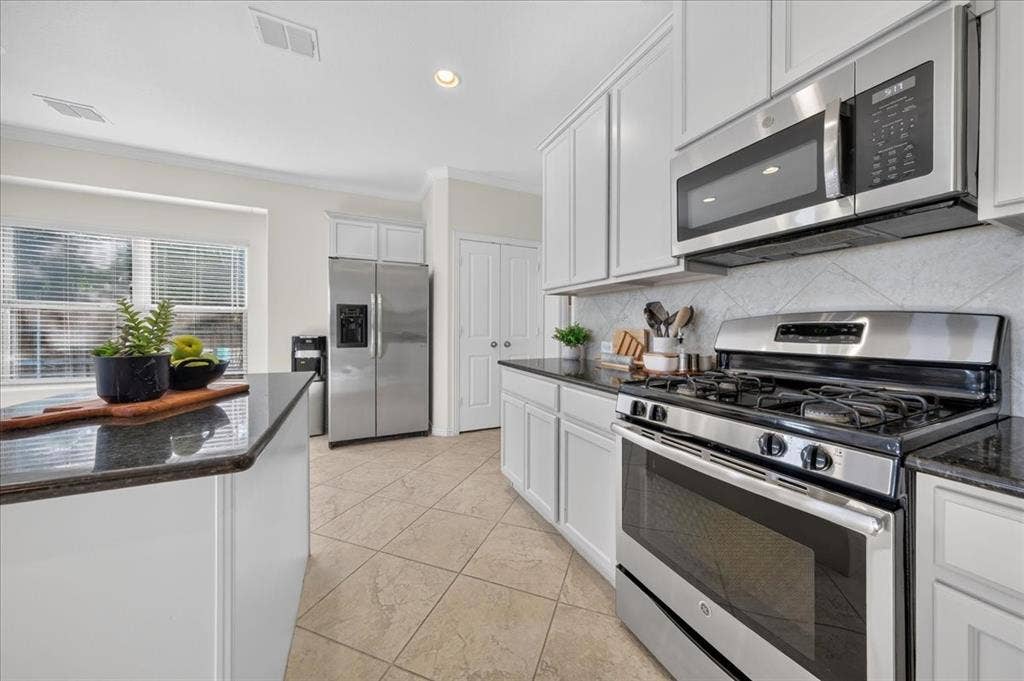 White cabinetry, stainless steel appliances, dark countertops, tiled backsplash, and tiled flooring