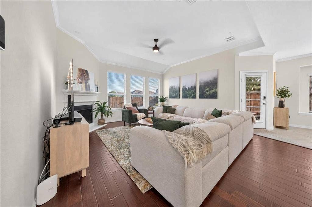Spacious living area featuring rich wood-finish flooring, a white mantel fireplace, and a ceiling fan