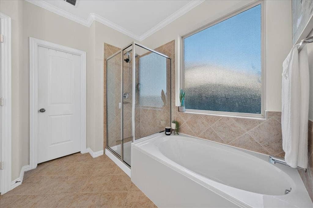 Built-in soaking tub, glass-enclosed shower, large privacy window, and neutral-toned floor tiling