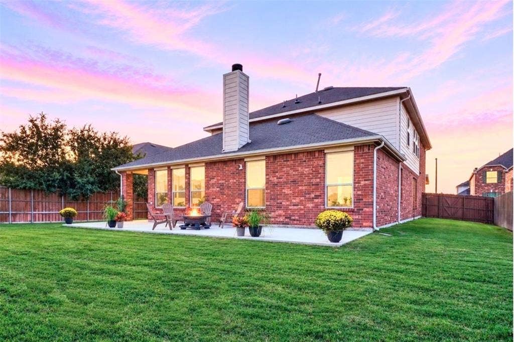 Expansive green lawn with a concrete patio, brick exterior, and a covered back porch