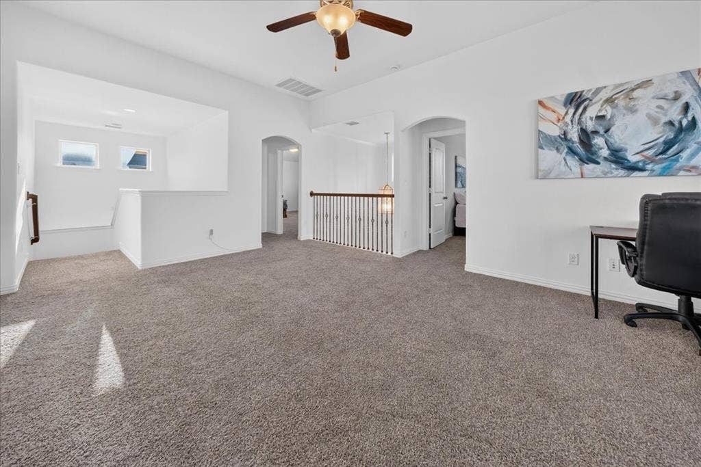 Carpeted floor, archways, white walls, ceiling fan, and staircase with wood handrail