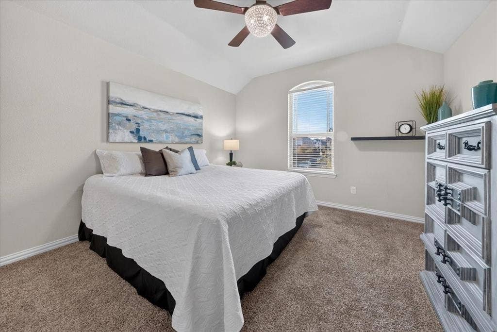 Vaulted ceiling, arched window, carpeted flooring, and a ceiling fan with integrated lighting