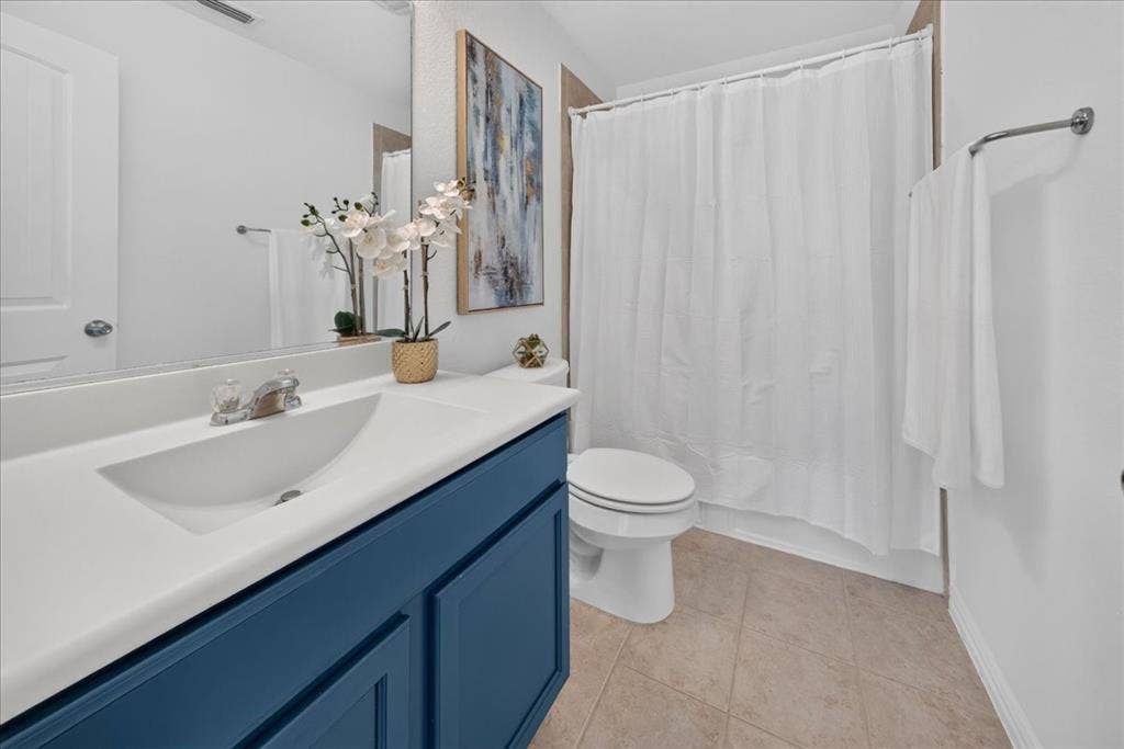 White vanity countertop with an integrated sink, blue-painted vanity cabinetry, and neutral-toned tile flooring