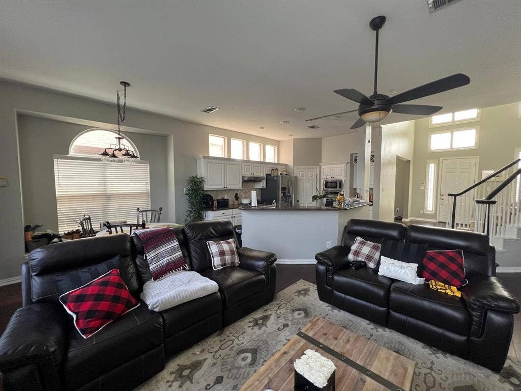 Open-concept living area featuring high ceilings, wood-finish flooring, a contemporary ceiling fan, a kitchen with white cabinetry and dark countertops, and a dining area with an arched window