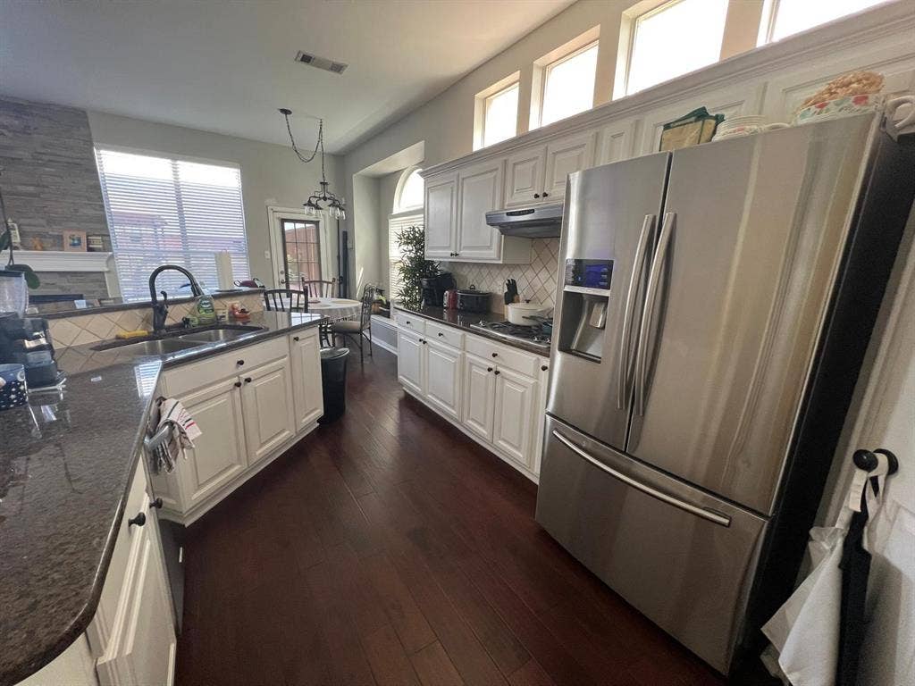Gourmet kitchen featuring dark wood-finish flooring, white cabinetry, dark countertops, a tile backsplash, and stainless steel appliances