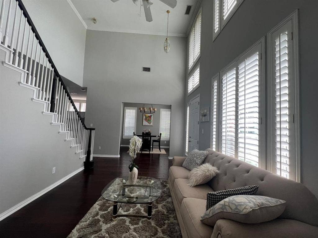 Living area featuring a two-story ceiling, dark wood-finish flooring, and a staircase with white balusters and a dark handrail