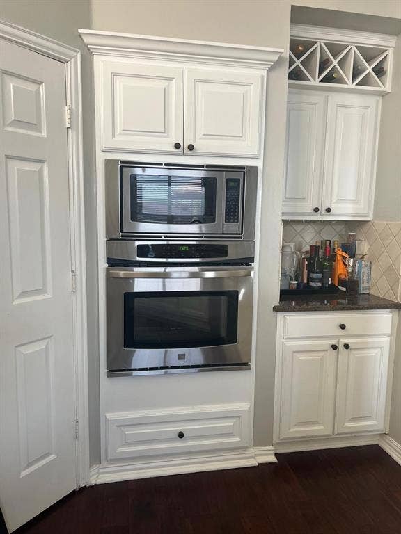 Built-in stainless steel microwave and oven combination with custom white cabinetry, crown molding, a lower storage drawer, and dark wood-finish flooring