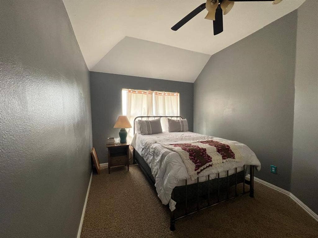 Carpeted room featuring a vaulted ceiling and a window with curtains
