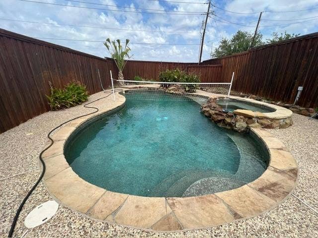 Curved swimming pool with an integrated spa featuring stone coping and a rock waterfall accent