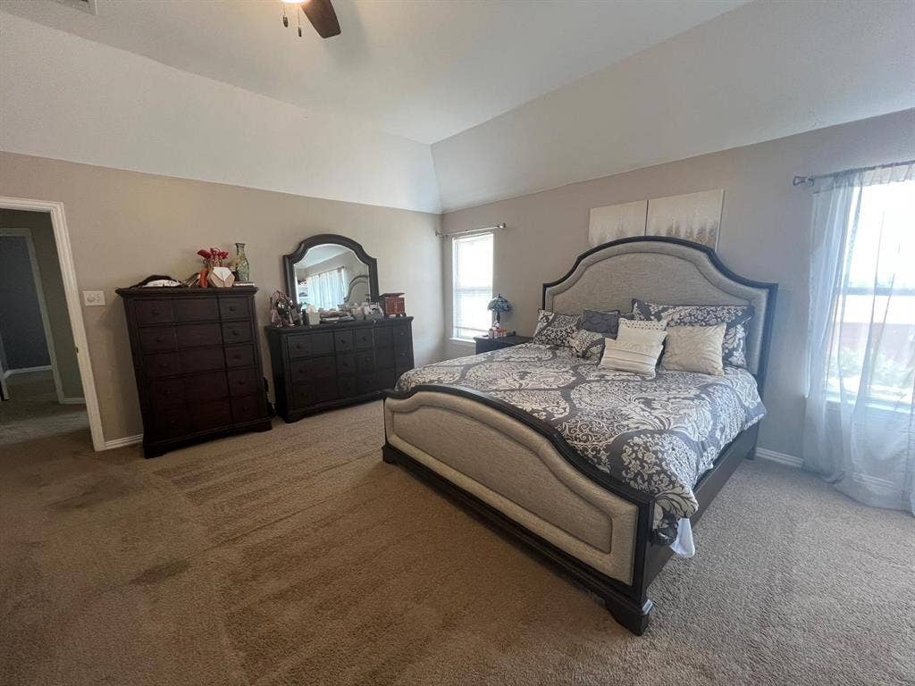 Spacious room featuring vaulted ceilings, light-toned wall paint, neutral carpeting, and a ceiling fan