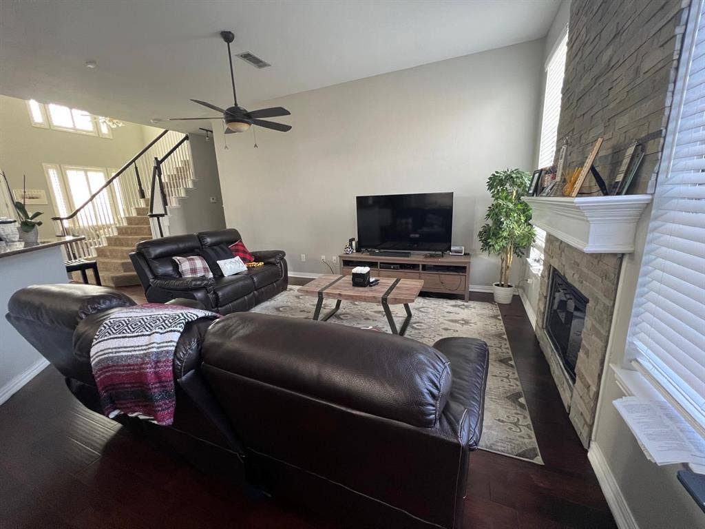 Vaulted ceiling living area featuring a stacked stone fireplace with white mantel, dark wood-finish flooring, and a ceiling fan