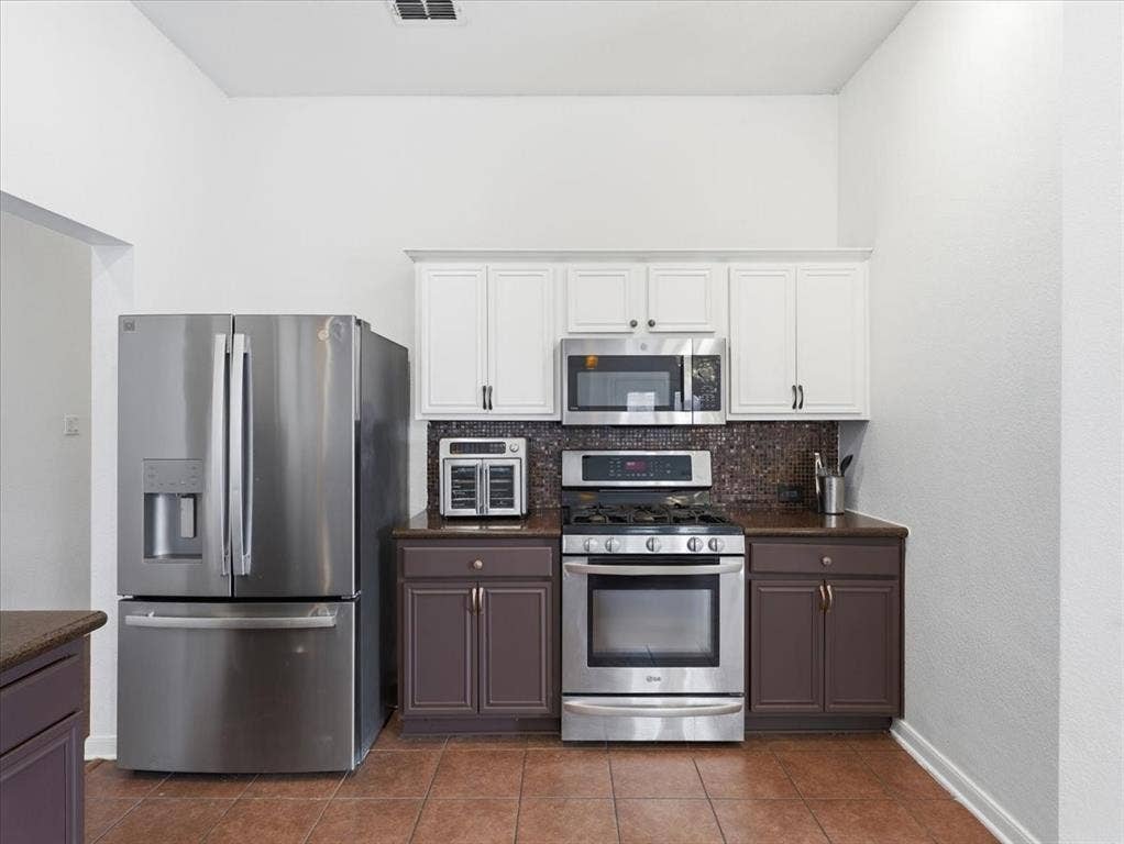 1039 Wood Brook Drive, Grand Prairie, TX 75052 Kitchen featuring stainless steel appliances, mosaic tile backsplash, and two-tone cabinetry