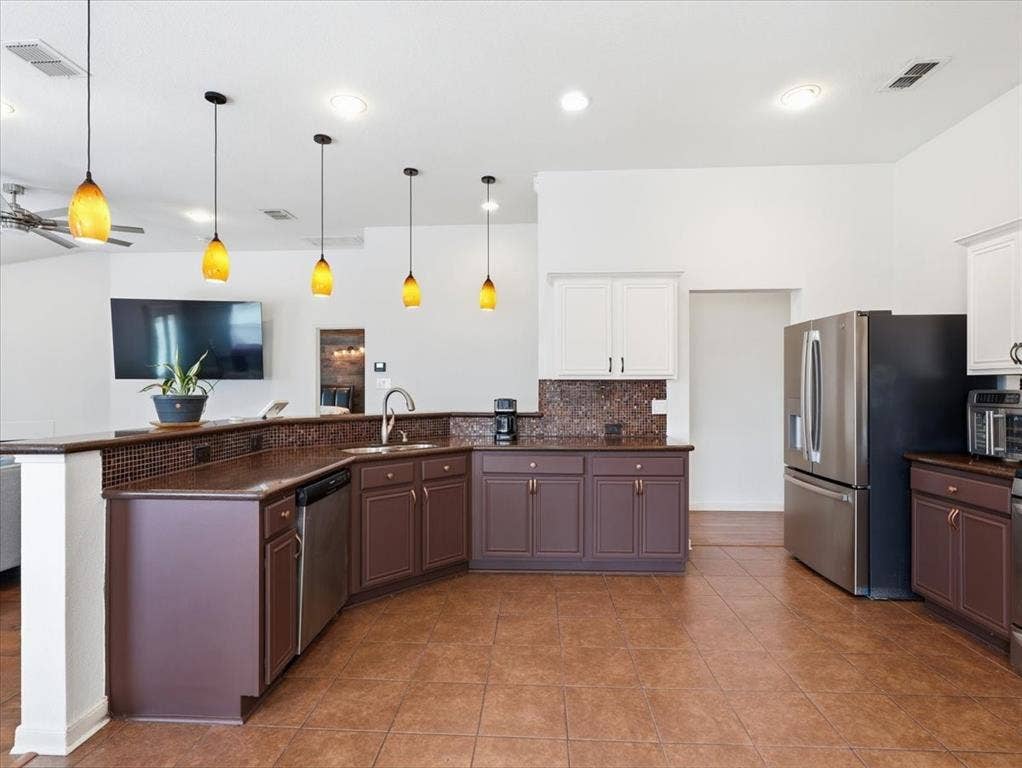 1039 Wood Brook Drive, Grand Prairie, TX 75052 Spacious kitchen featuring a large tile floor, dark wood-finish cabinetry, light upper cabinetry, stainless steel appliances, and a mosaic tile backsplash